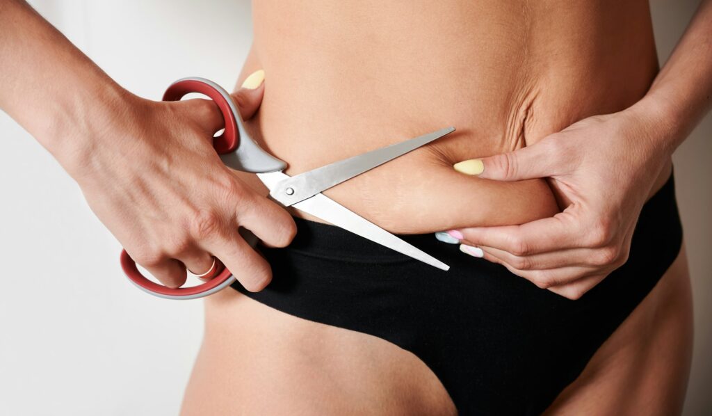 Young woman cutting off excess fat with scissors.