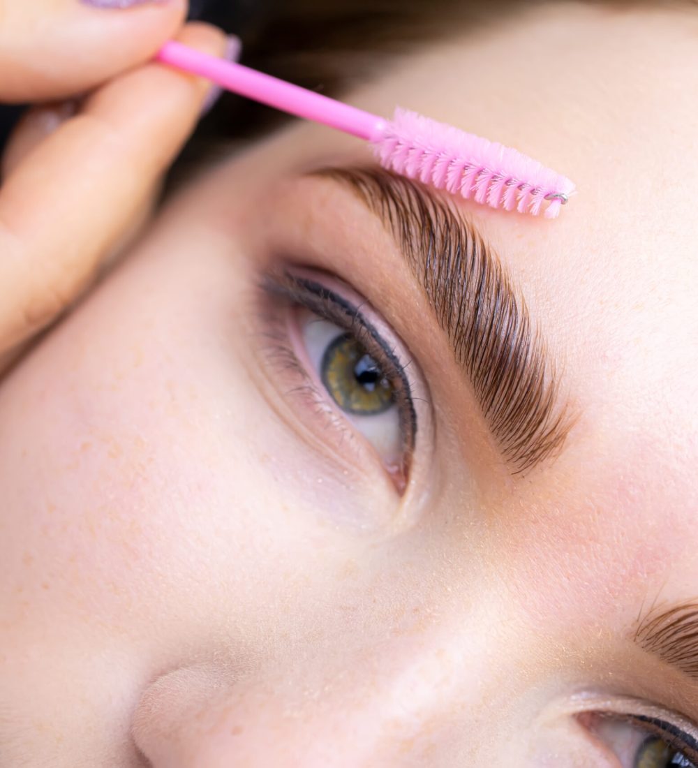 macro photography of the model's hairs the master combs the eyebrow hairs with a pink brush after the procedure long-term styling and lamination