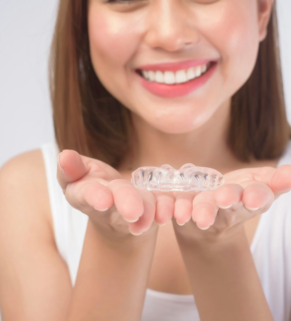 Young smiling woman holding invisalign braces over white background studio, dental healthcare